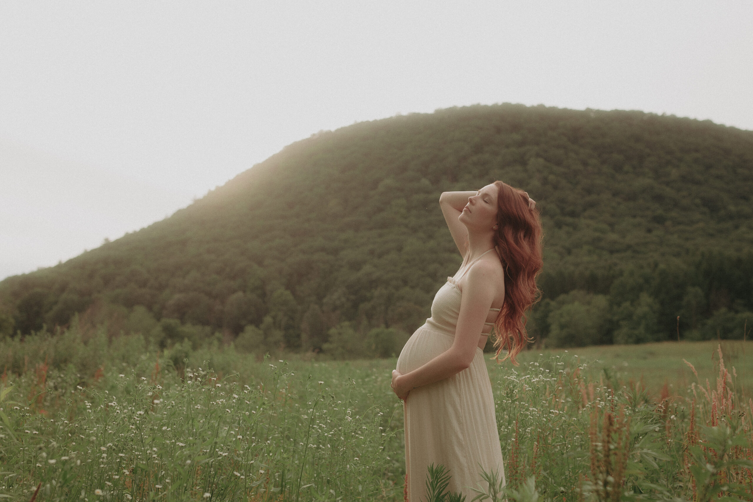 Pregnancy photo in a field of wildflowers with a hill in the background