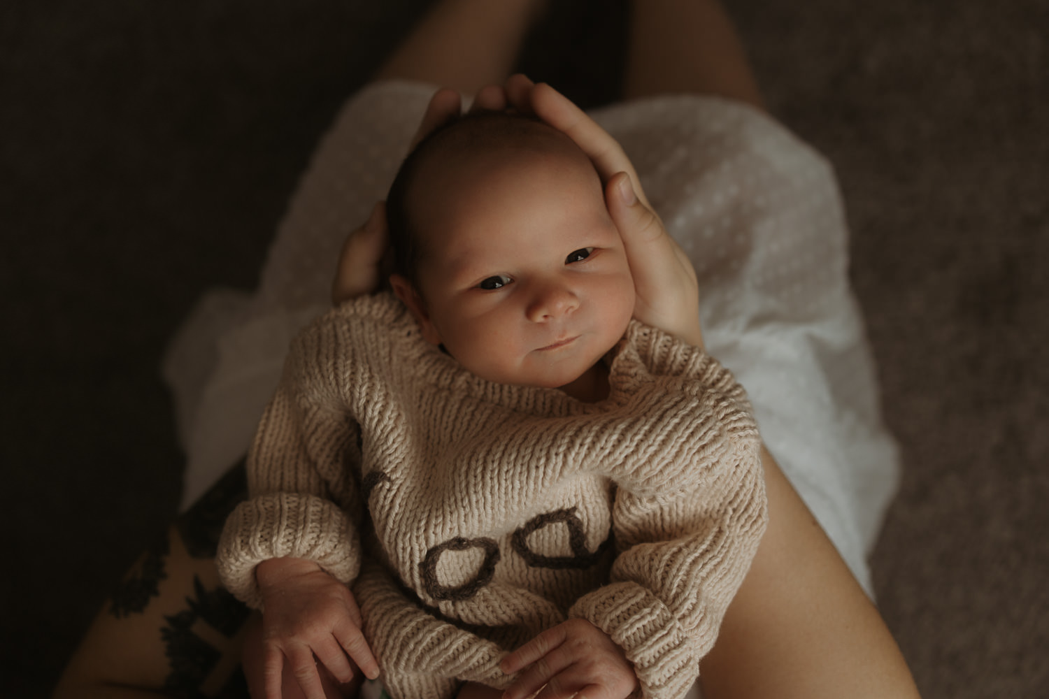 Cozy newborn in knitted sweater is being held by his Mother during a newborn photo session in Rochester NY